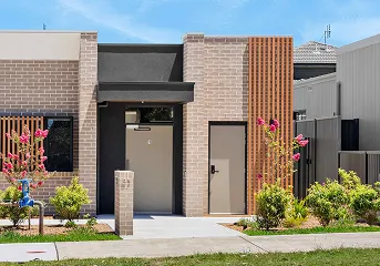Modern brick house entrance with black door, wooden slat feature, and landscaped garden with pink flowering plants.