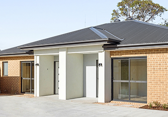 Modern single-story brick house with dark roof, white entrance, and large windows.