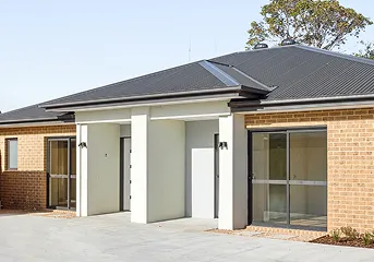 Modern single-story brick house with dark roof, white entrance, and large windows.