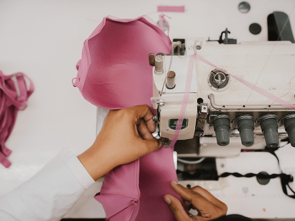 Close-up of hands sewing pink fabric using an industrial sewing machine.