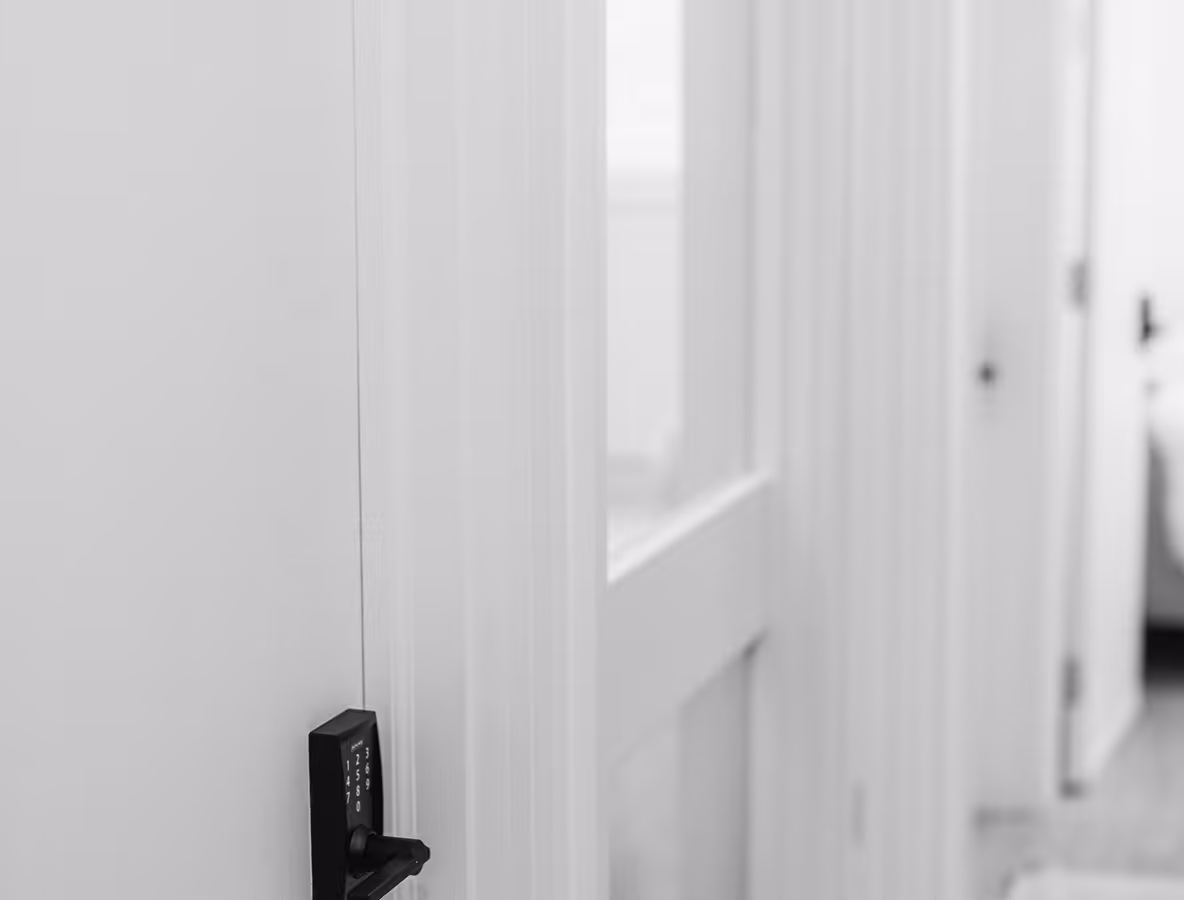 Minimalist hallway with white walls and doors, featuring a black keypad door lock on the left door, shot in black and white.