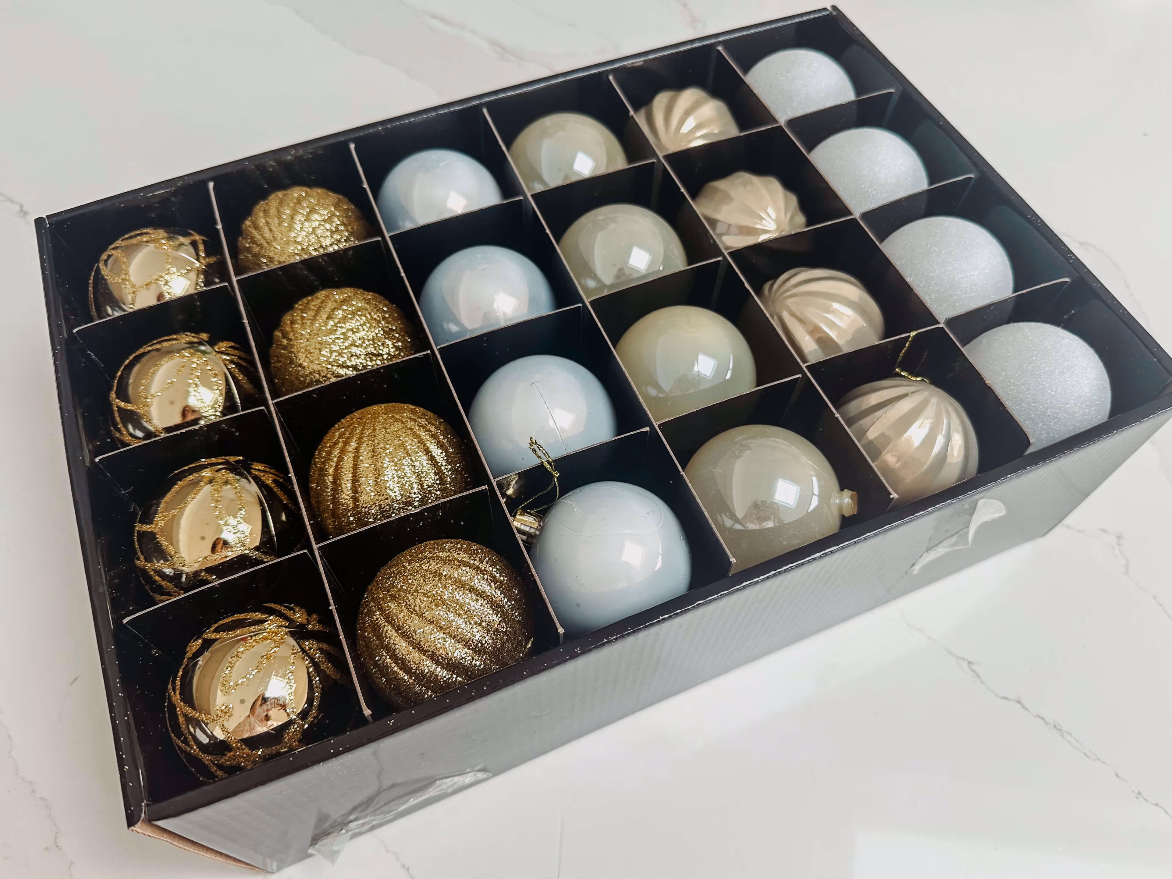 White and gold shatterproof baubles in various shapes and sizes adorn a snow flocked Christmas tree, complementing the soft grey and warm wood tones of the room