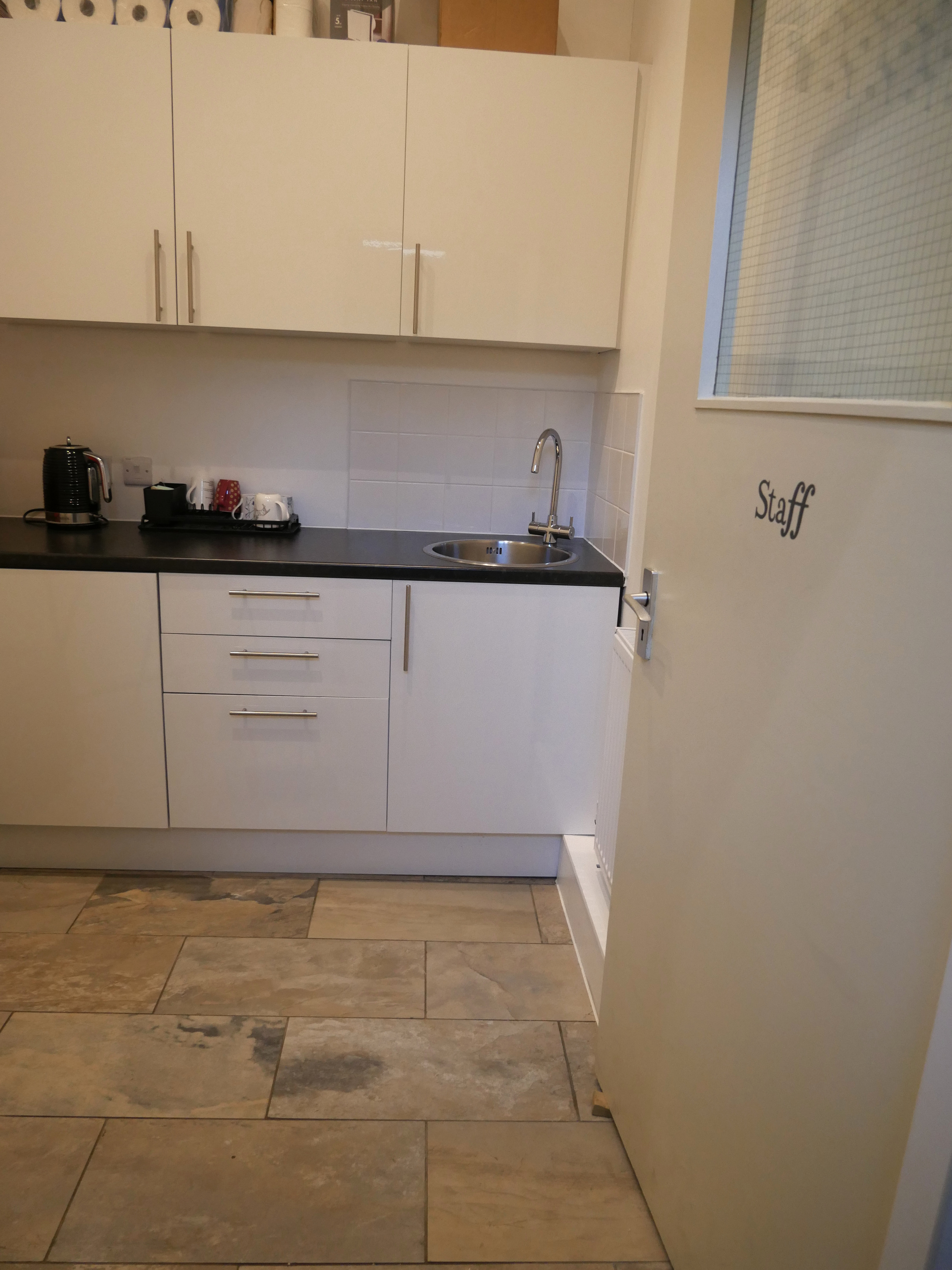 The finished staff room tea point, with white cupboards, a black worktop, sink and kettle.