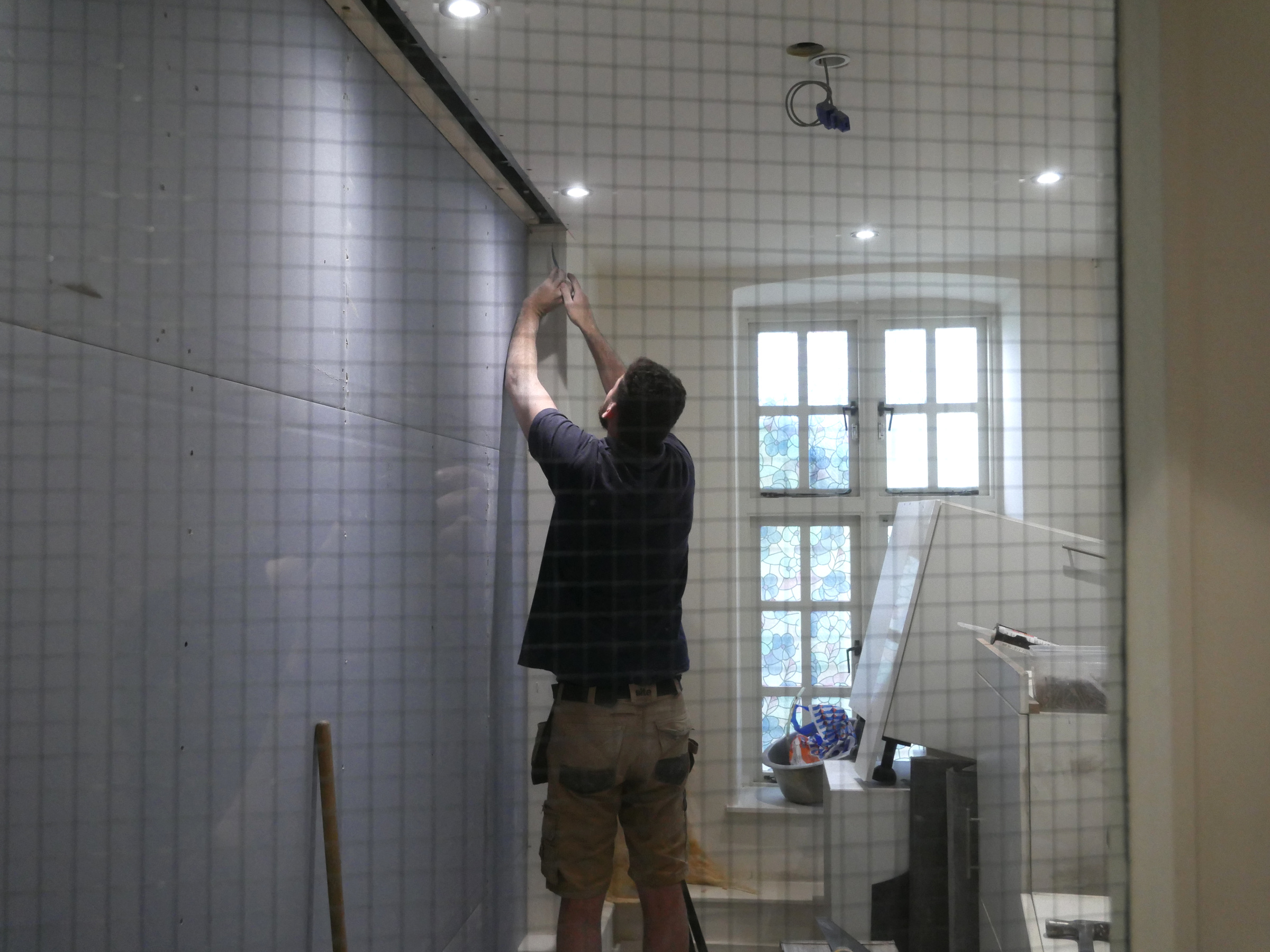 A builder works on the acoustic wall during refurbishment at The Stables, seen through a wired-glass window.