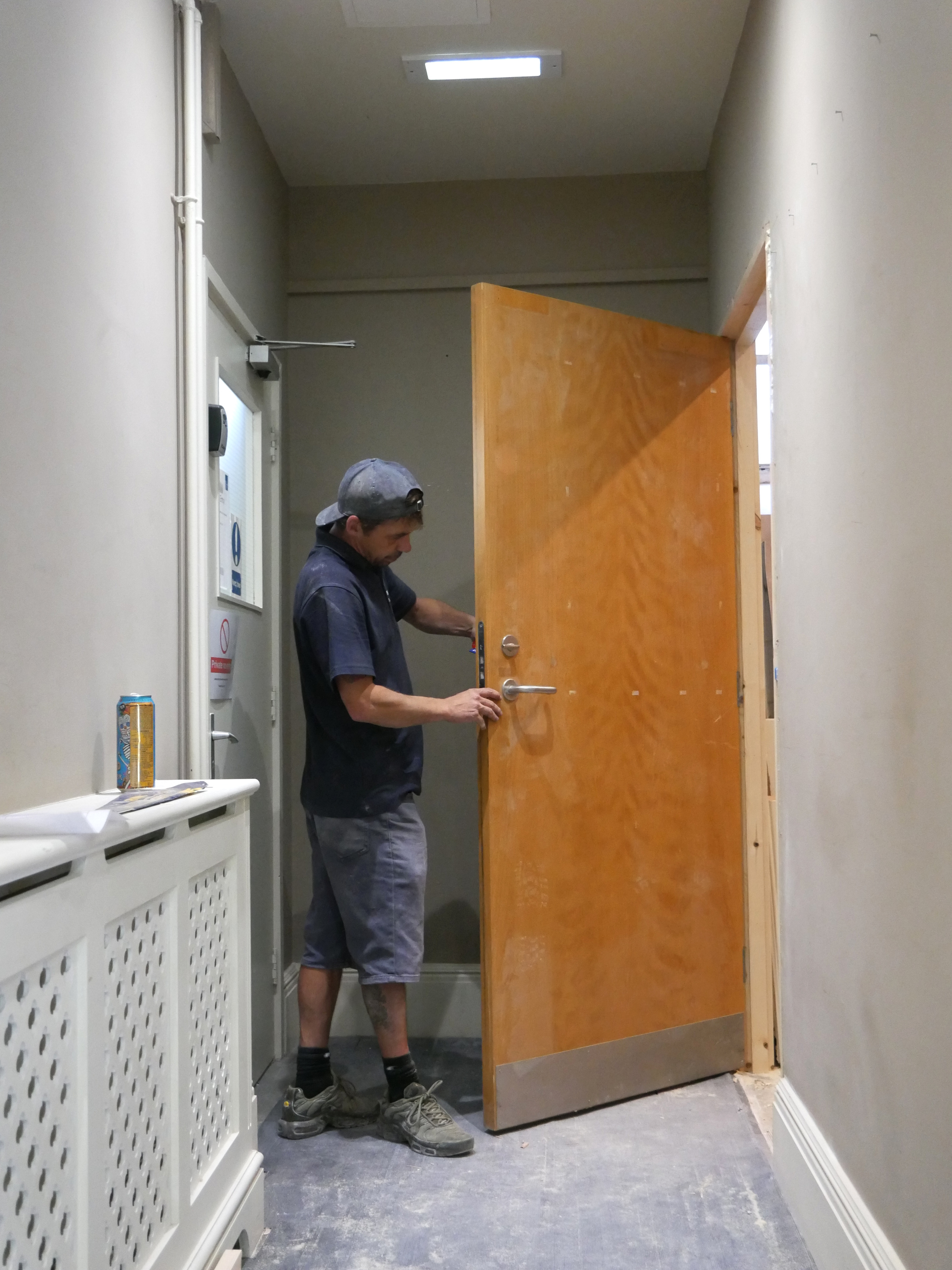 A builder adjusts a wooden door during refurbishment work in the corridor at The Stables.