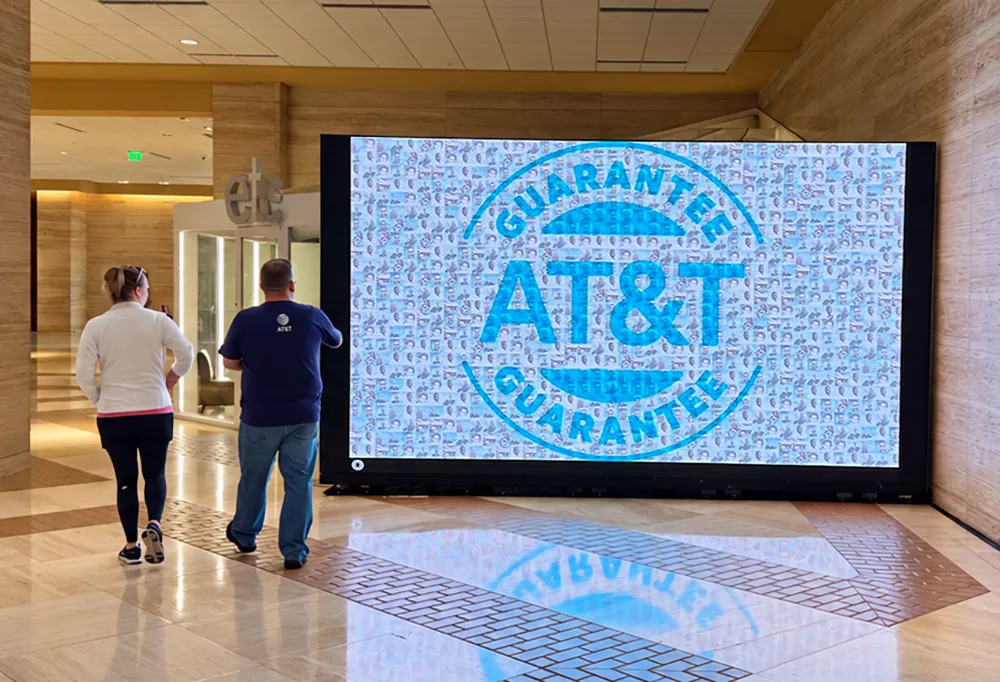 Live photo mosaic of guest photos forming the AT&T Guarantee logo on a large LED wall in a hotel corridor