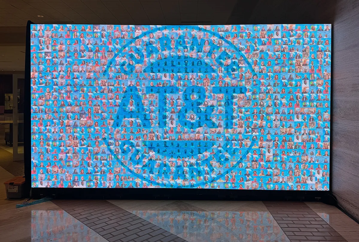 A large digital display screen with a branded photo mosaic in the middle of an event venue