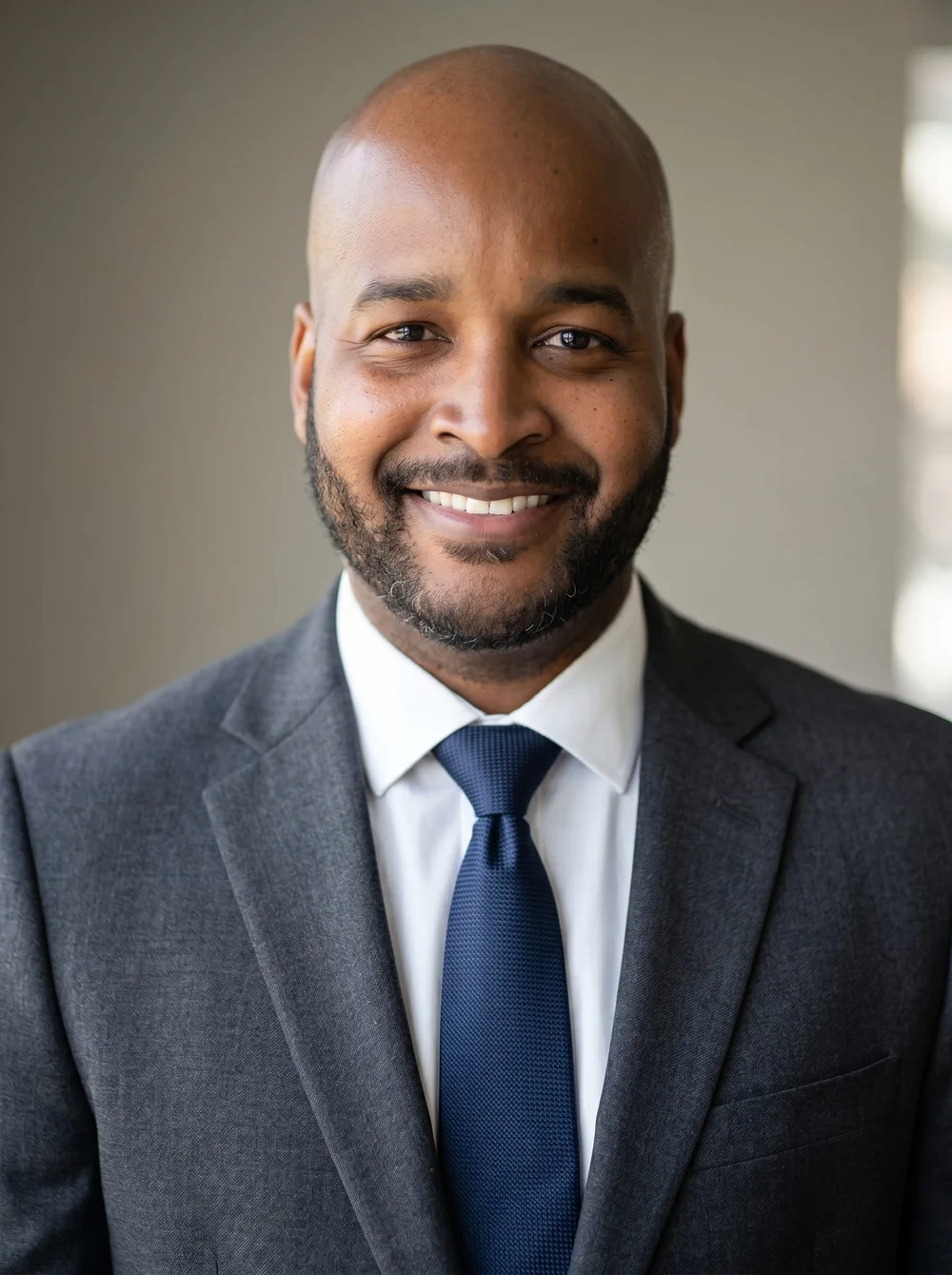 AI-enhanced professional headshot of a smiling guest in a gray suit and navy tie