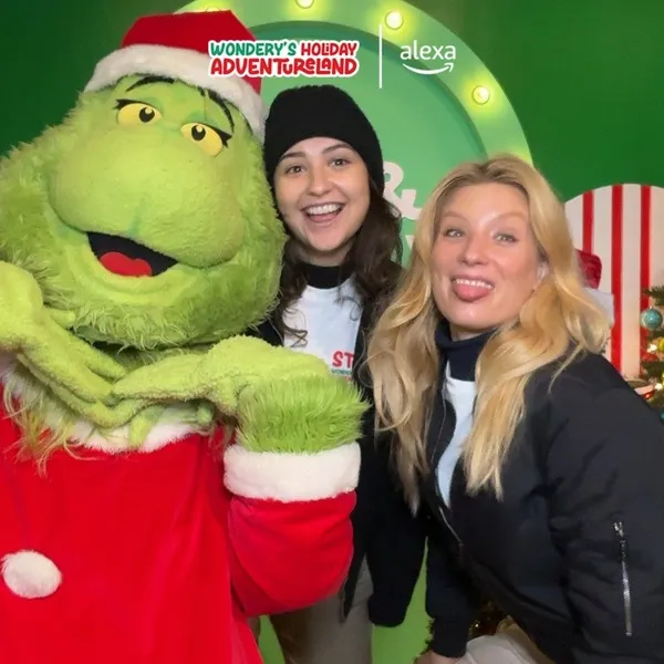 Photo booth snapshot of two guests posing with the Grinch on a Wondery Holiday Adventureland frame with Alexa branding