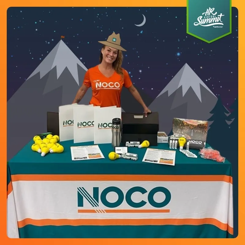Photo booth snapshot of an exhibitor behind a NOCO booth table on an HR Summit frame