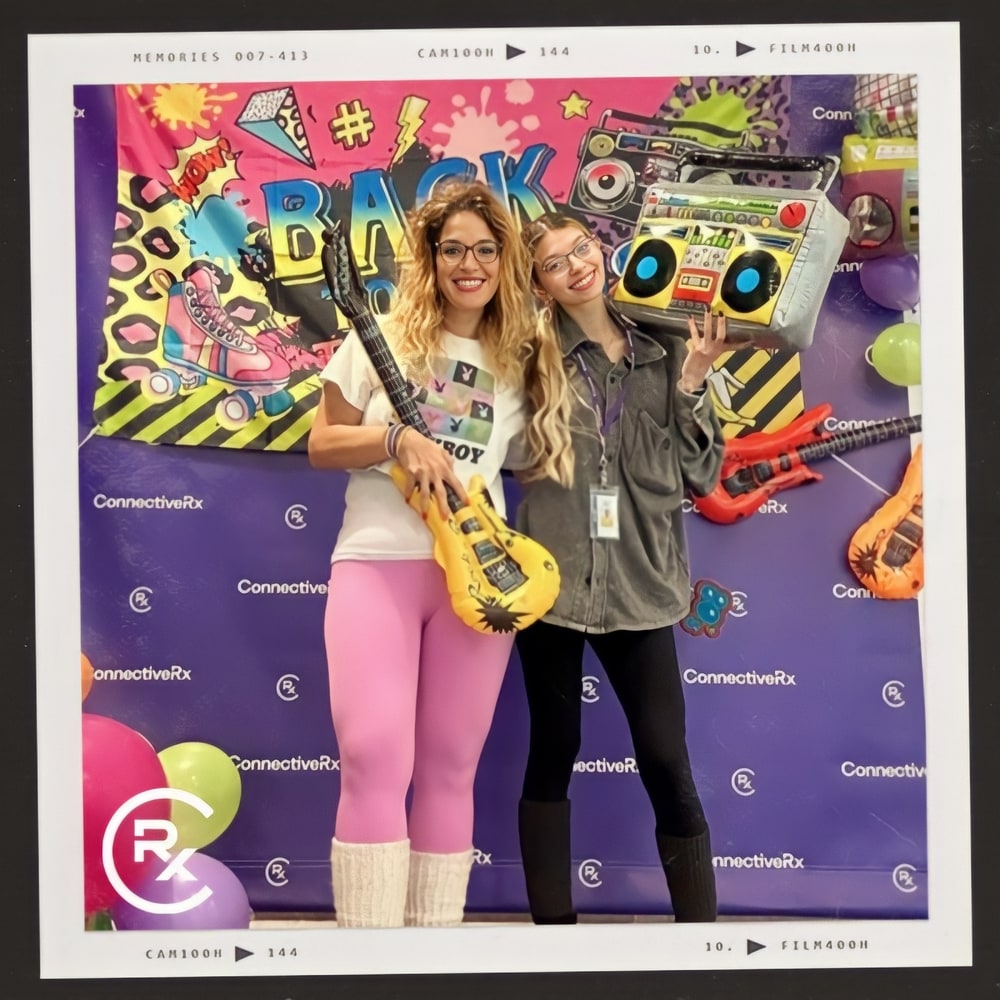 Photo booth snapshot of two guests with inflatable guitars and boomboxes on a ConnectiveRx 90s party frame
