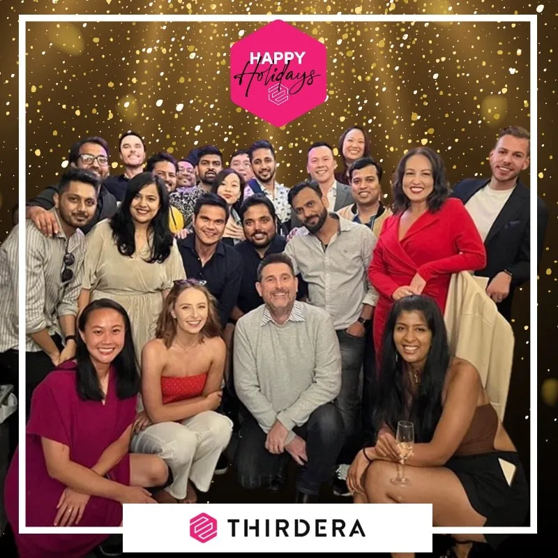 Photo booth snapshot of a large team on a gold confetti Thirdera Happy Holidays frame