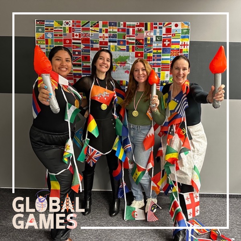 Photo booth snapshot of four teammates draped in flags holding torches on a Global Games frame