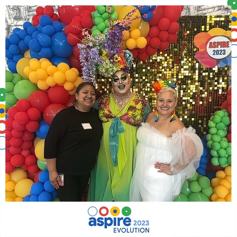 Photo booth snapshot of three guests before a rainbow balloon arch on an Aspire 2023 Evolution frame