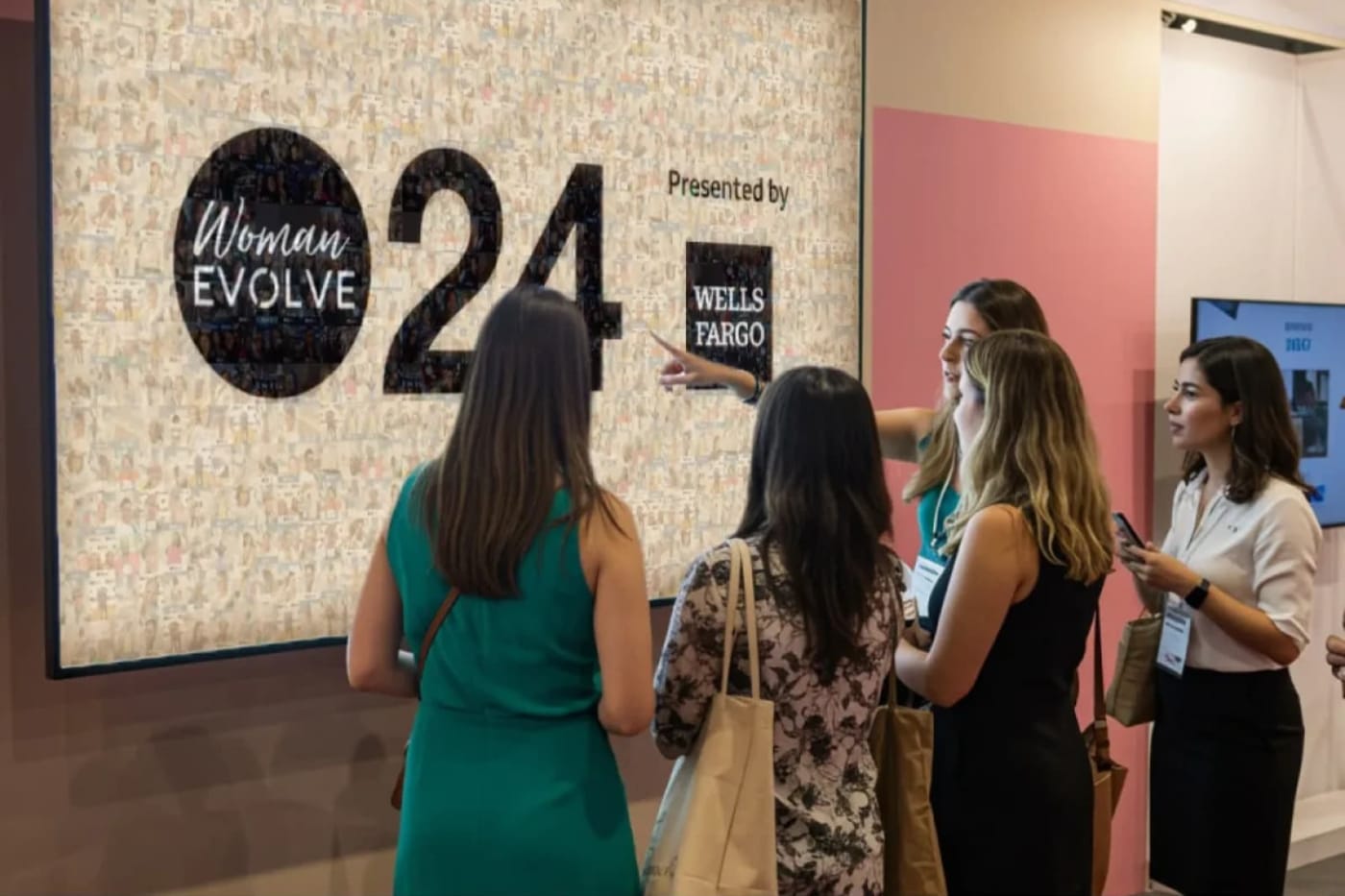 Four attendees at a branded photo mosaic wall in an expo hall, one pointing out a single photo tile.