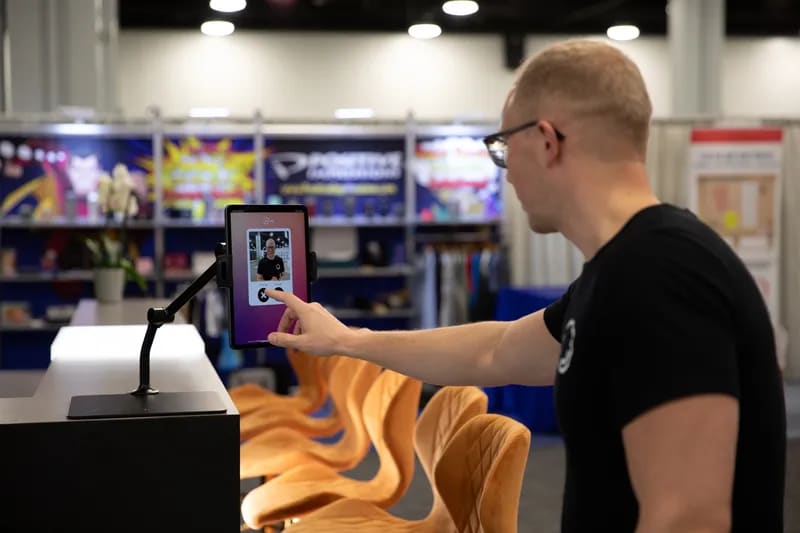 A guest taps a tablet mounted on an arm stand at a trade show booth to start an experience
