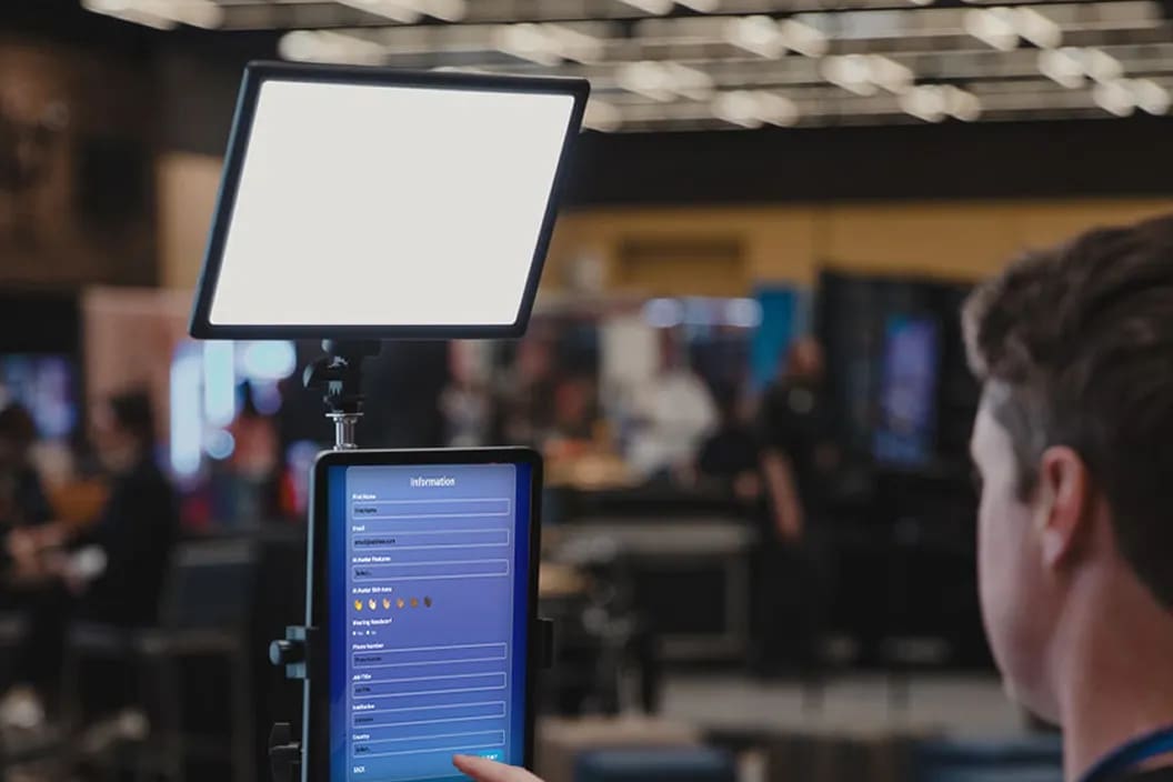 A guest reaching for a tablet mounted on a floor stand under an LED light panel at an event capture point