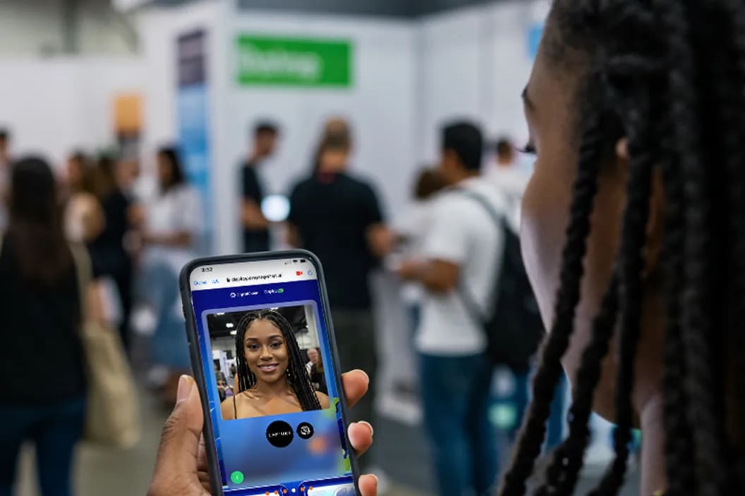 A guest on a trade show floor holding her phone with the branded activation open in her browser, showing her portrait