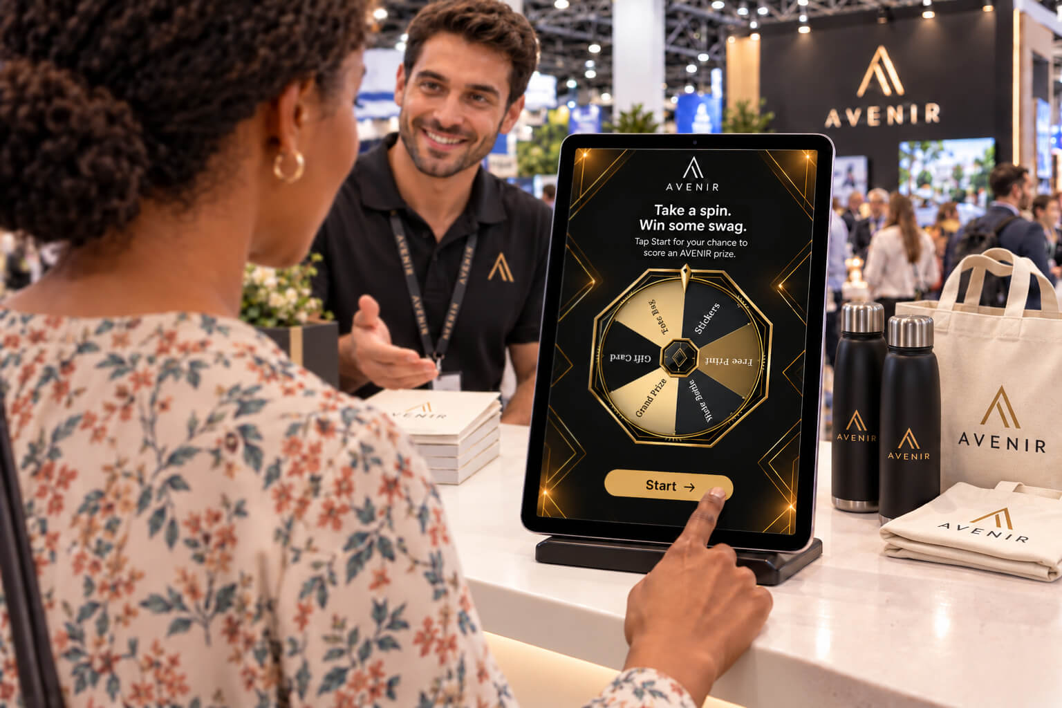 Tablet on a booth counter showing a branded prize wheel entry screen, with a visitor tapping Start as a trade show crowd mingles behind