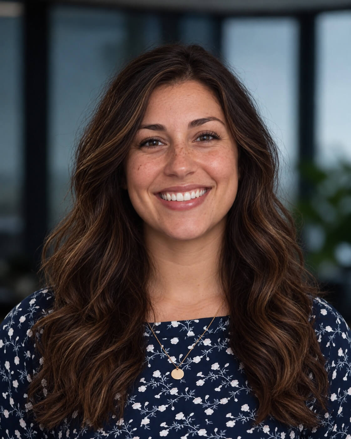 AI event headshot: smiling woman with long wavy brown hair in a navy floral blouse against a blurred office background