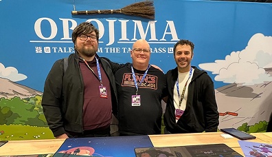 Three men standing behind a table with game artwork in front of an OROJIMA promotional backdrop.