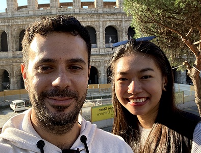 Smiling man and woman posing for selfie with Rome's Colosseum in bright daylight behind them.