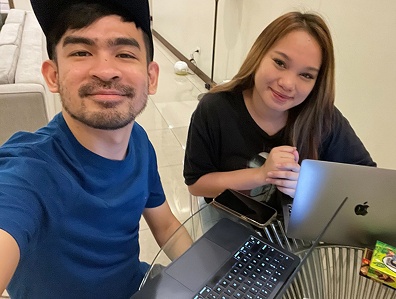 Two people smiling at a table with laptops and a smartphone in an indoor setting.