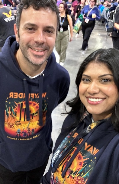 Smiling man and woman with mask posing for selfie at a busy indoor event or convention.