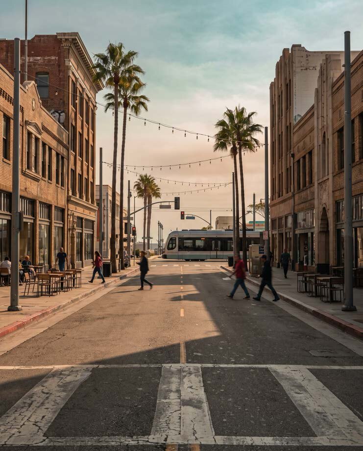Downtown Long Beach street with palm trees and a Metro train at sunset