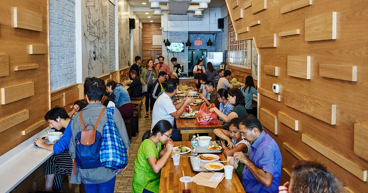 Busy casual restaurant interior with diverse people eating and socializing at wooden tables.