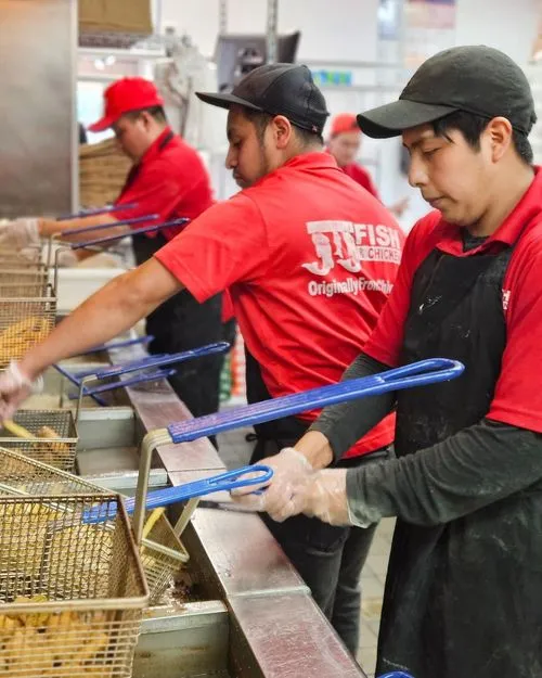 Three workers in red shirts and black aprons frying food in baskets at a commercial kitchen fryer station.