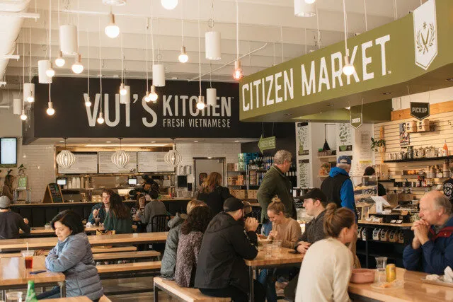 Interior of Vui's Kitchen Fresh Vietnamese at Citizen Market with people sitting at wooden tables and ordering at the counter.