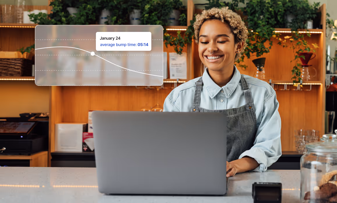 Smiling restaurant manager using laptop with overlaid kitchen performance chart.