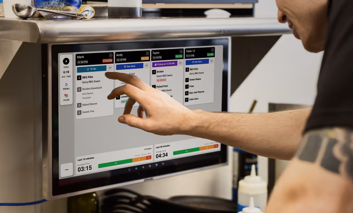 Person pointing to kitchen display showing 15- and 30-minute performance metrics with on-time, caution, and late orders.