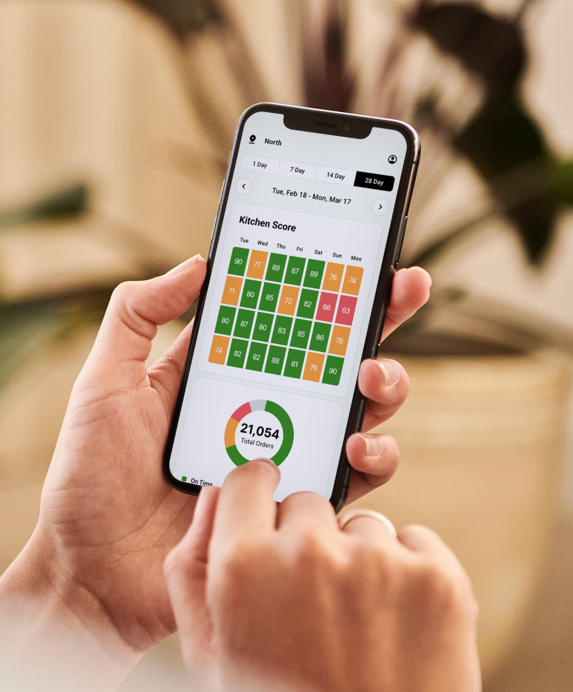 Hand holding phone displaying Fresh KDS Kitchen Score of 87 with performance breakdown.