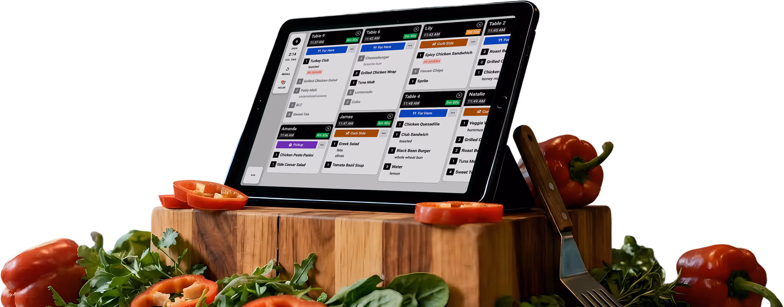 Tablet displaying a restaurant order management system on a wooden cutting board with sliced red bell peppers, leafy greens, a fork, and whole bell peppers around it.