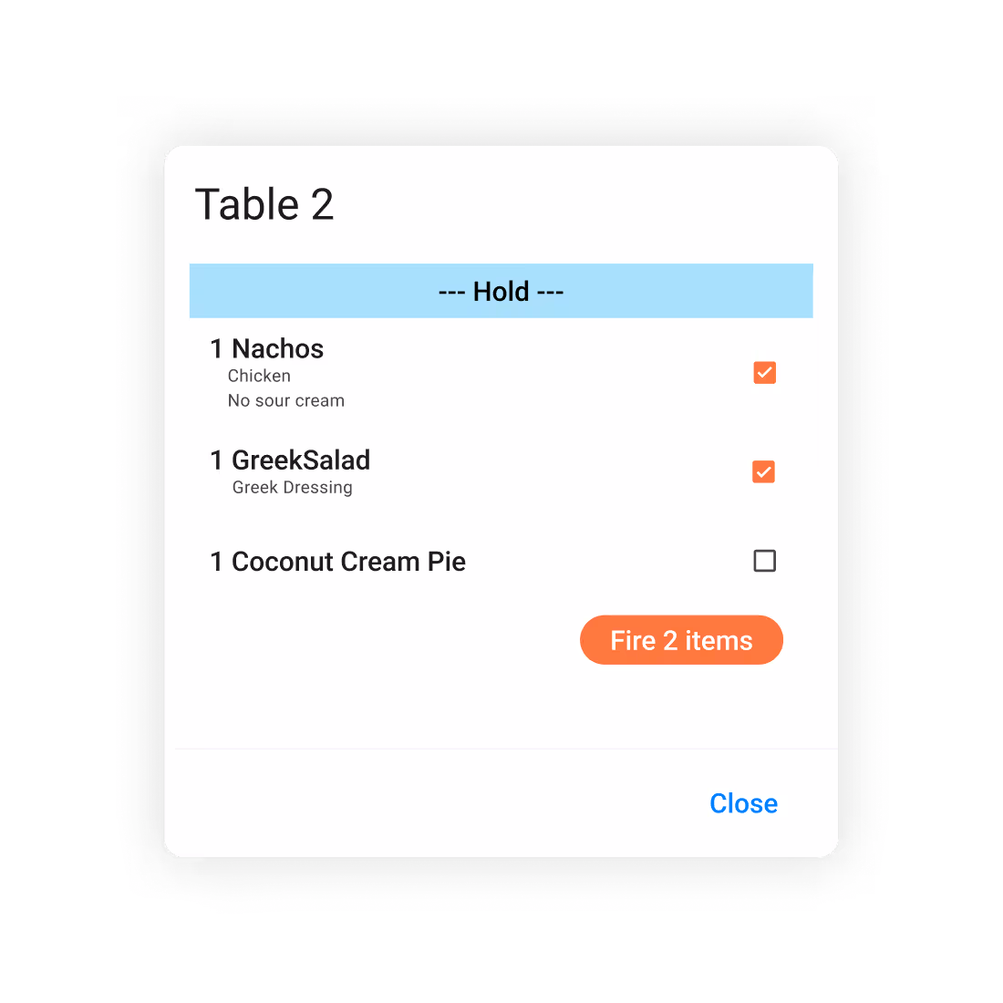 Order hold screen titled Table 2 showing 1 Nachos with chicken and no sour cream, 1 Greek Salad with Greek dressing checked to fire, and 1 Coconut Cream Pie unchecked, with an orange button labeled Fire 2 items and a Close link.