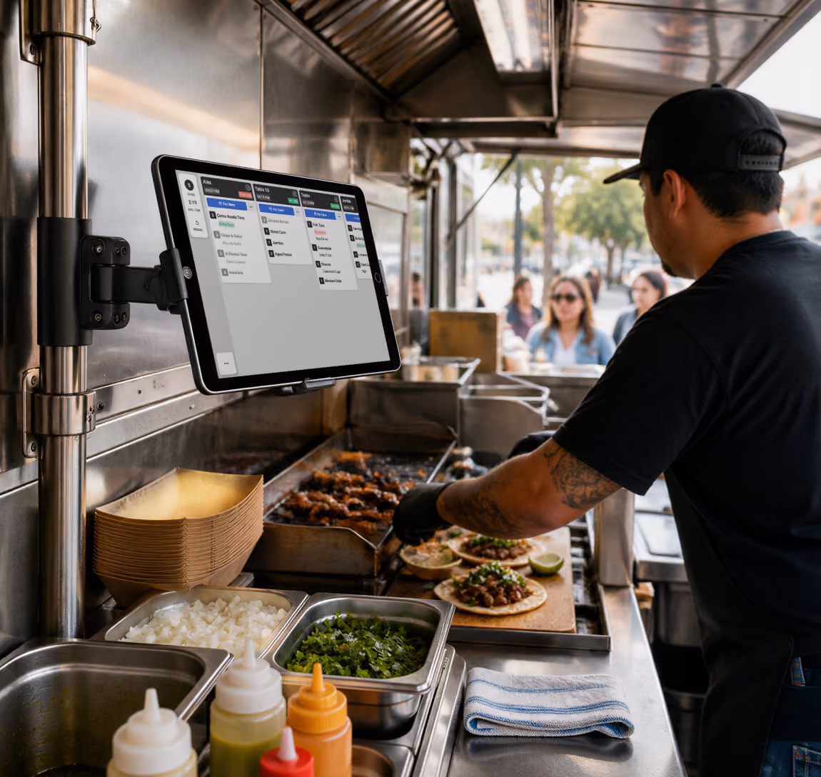 Man preparing tacos inside a food truck, with ingredients and a mounted Fresh KDS screen showing orders.