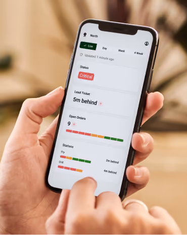 Hand holding a smartphone showing a status report with lead and station delays in the On The Fly app.