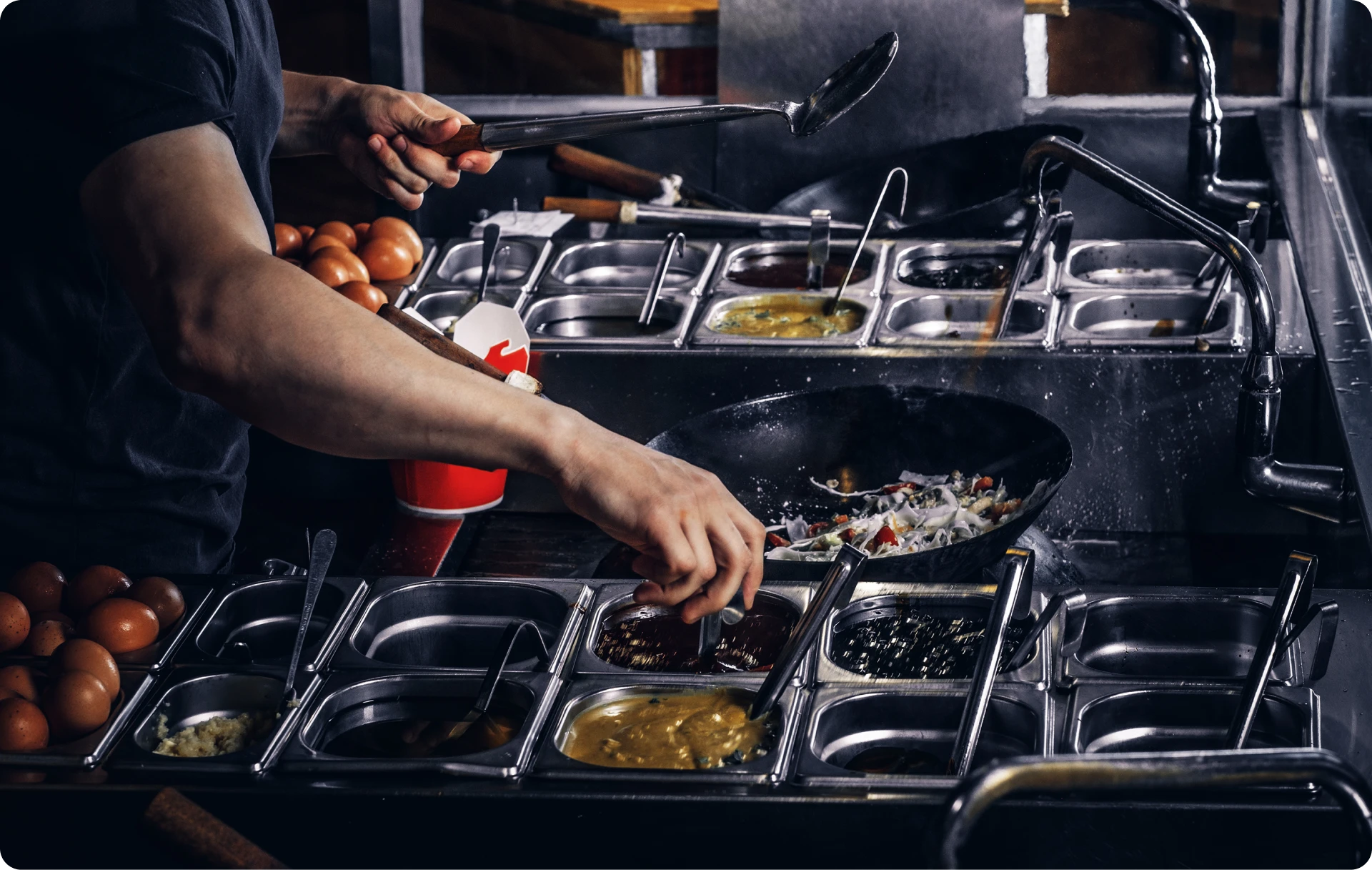 Restaurant line cook working a busy kitchen station with organized mise en place and multiple prep containers