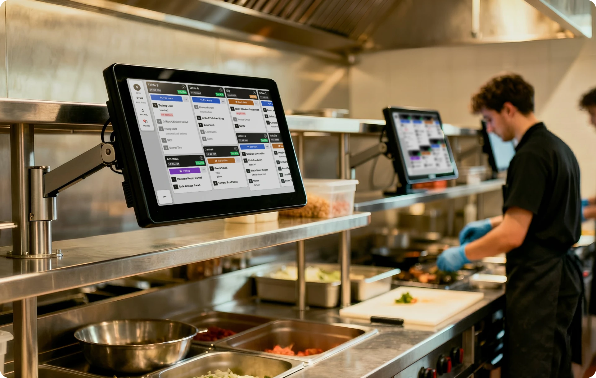Fresh KDS kitchen display system showing active orders on a restaurant kitchen line with a cook working in the background