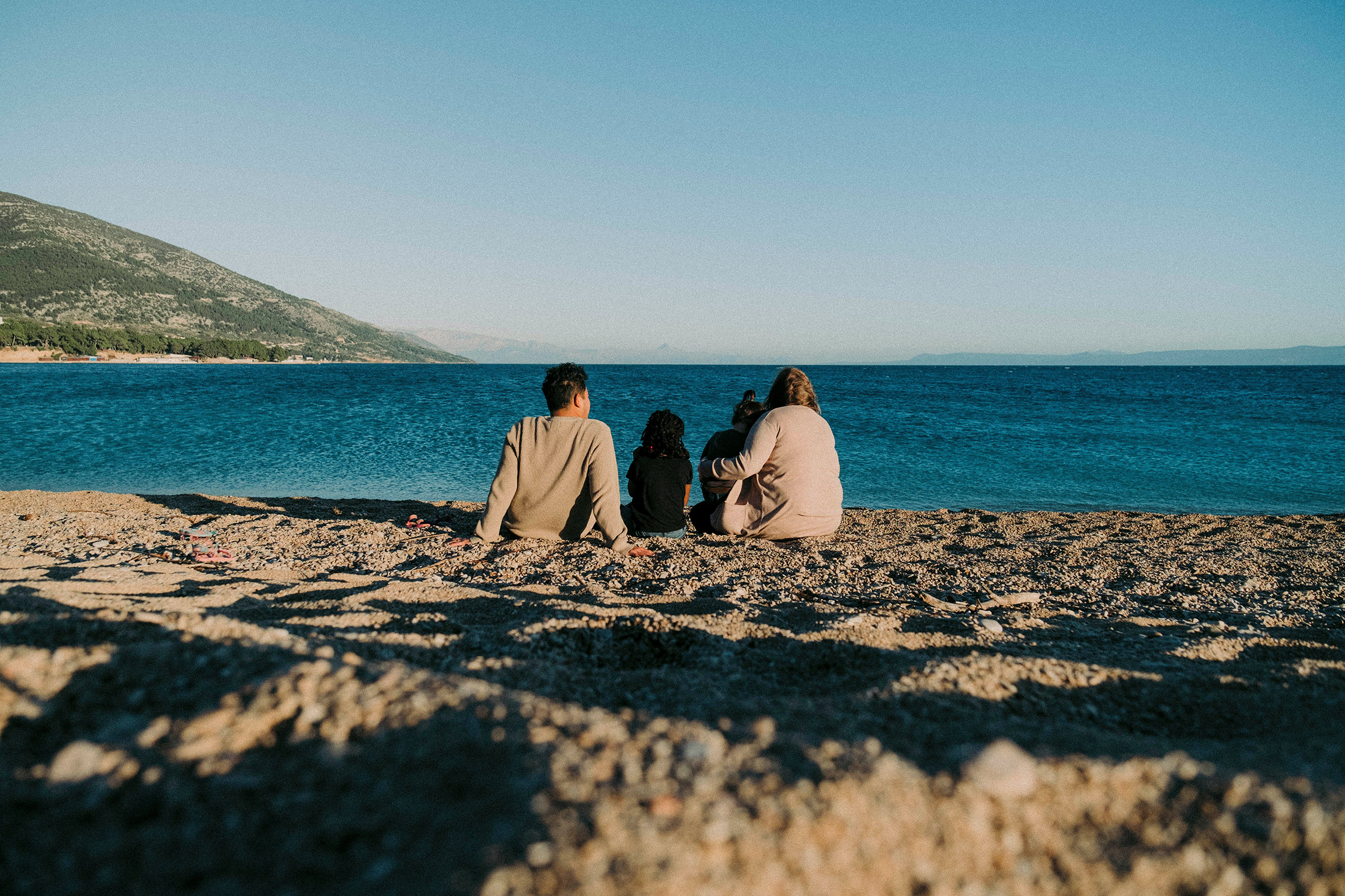 Photo of two adults and two kids seated together on a beach overlooking water