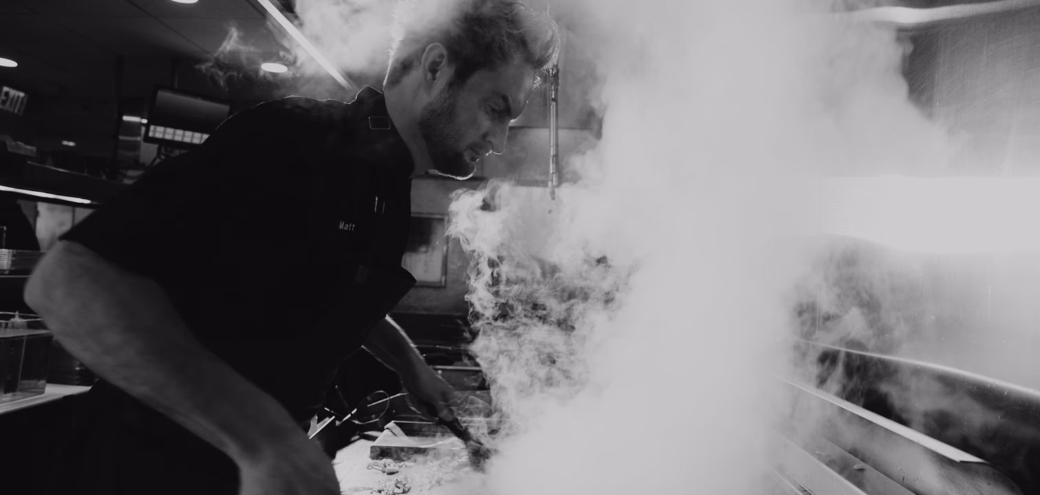 Chef Matt cooking intensely amid a large cloud of smoke in a restaurant kitchen.