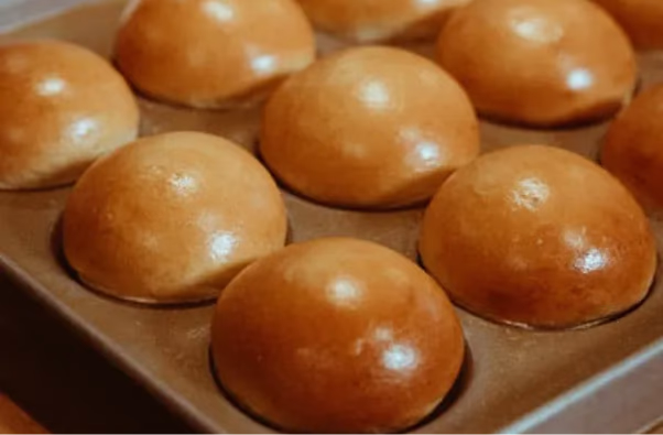 Golden-brown dinner rolls baking in a muffin tin.