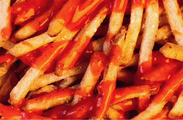 Close-up of crispy French fries topped with red ketchup sauce.