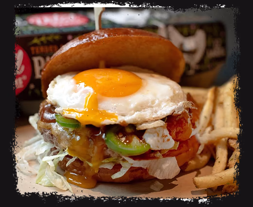 Burger with sunny-side-up egg, lettuce, jalapeños, tomato, and melted cheese with fries on the side.