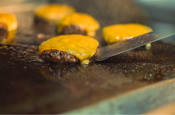 Close-up of a cooked beef burger patty topped with melted cheddar cheese on a grill.
