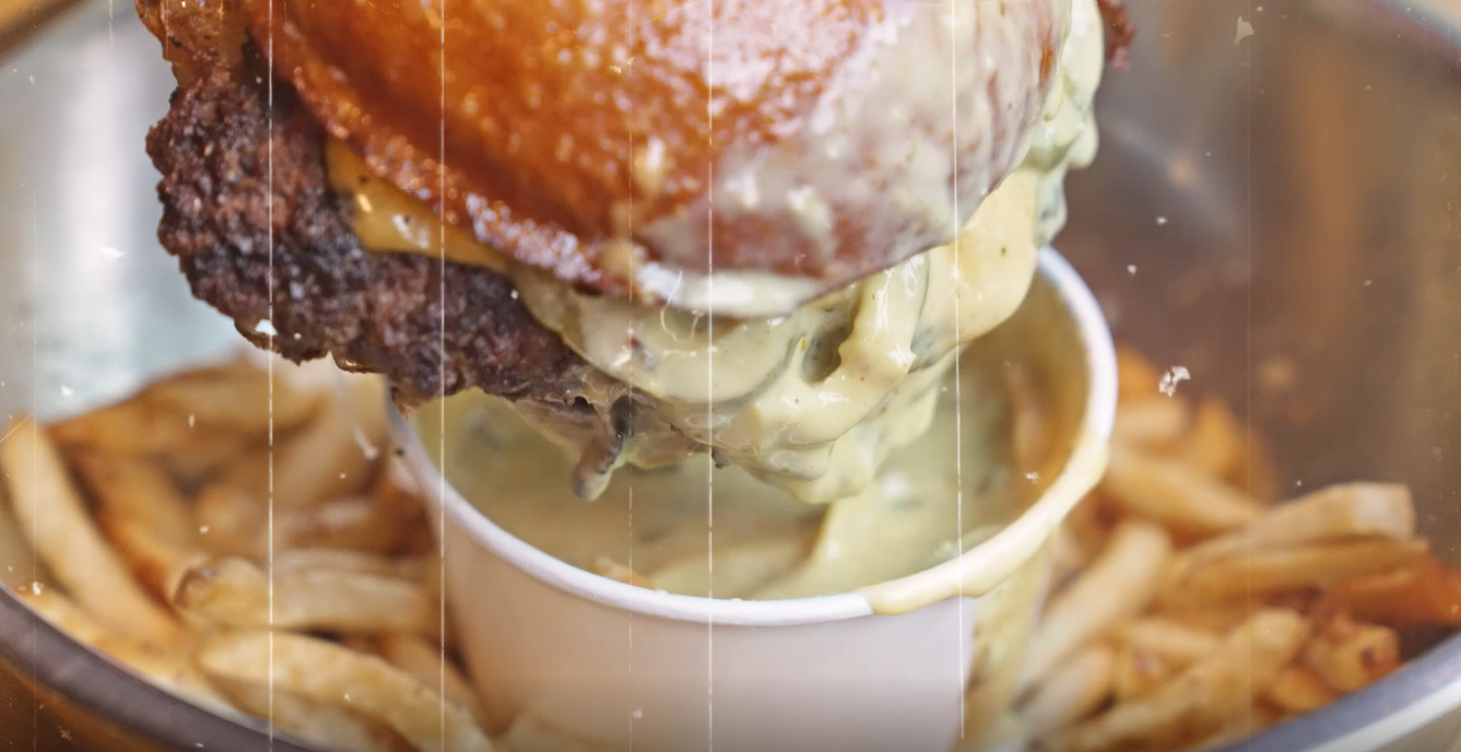 Wagyu Smash Burger being dipped into Fired Up Queso