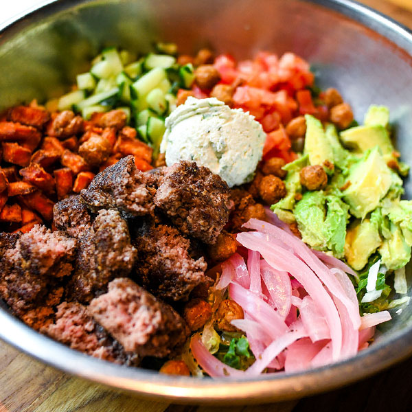 Burger bowl House greens tossed in oregano lemon vinaigrette, 100% Grass-Fed Pasture-Raised Beef, sweet potatoes, cucumbers, tomatoes, pickled red onions, avocado & spicy garbanzo beans with whipped jalapeño-cilantro goat cheese.