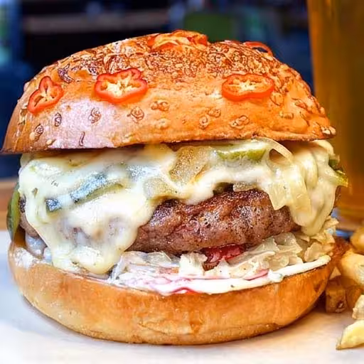 Beef Patty, Queso Fundido with Roasted Poblanos & Caramelized Onions, crisp Texas Slaw & Jalapeño Cilantro Aioli on a Fresno Cheddar Bun